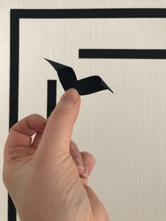 a hand is pointing at a piece of paper that looks like an origami bird