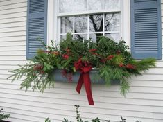 a window box filled with greenery and red bow on the side of a house