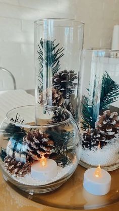 three glass vases with pine cones and candles on a table