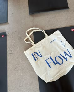 a white tote bag sitting on top of yoga mats with the words in flow printed on it