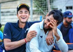 two men sitting next to each other with their arms around one another and smiling at the camera