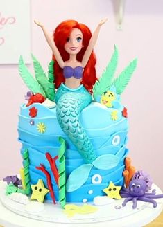 there is a little mermaid on top of a cake with sea life around it and under the waves