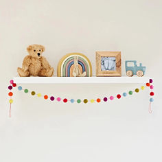 a teddy bear sitting on top of a white shelf next to a rainbow wall hanging