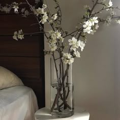 there is a vase with white flowers in it on the table next to a bed