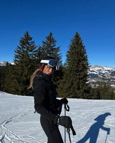 a woman standing on top of a snow covered slope wearing skis and goggles