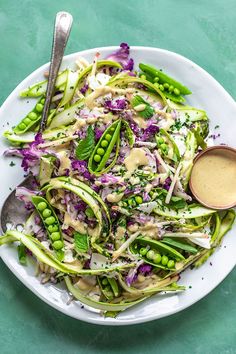 a white plate topped with green vegetables covered in dressing next to a fork and spoon