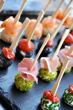 small appetizers are lined up on a black plate with toothpicks sticking out of them