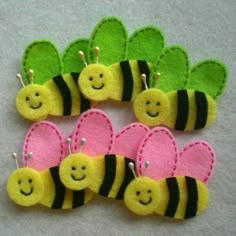 four felt bee brooches with hearts and smiling faces on them, sitting next to each other