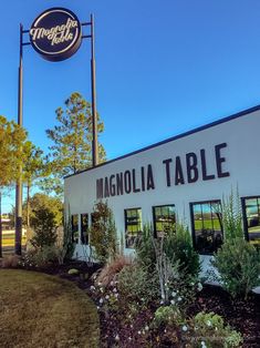 a sign that says magnolia table in front of a building with trees and bushes around it