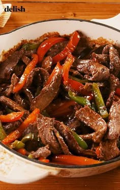 a pot filled with beef and peppers on top of a wooden table next to a fork