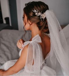 a woman sitting on top of a bed wearing a white veil and flower in her hair