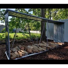 a small metal structure with logs in the ground next to trees and a building behind it