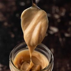 a spoon full of peanut butter on top of a jar filled with caramel sauce