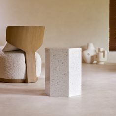 a white chair sitting on top of a floor next to a cement block in front of a window