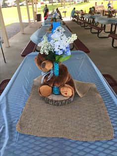 a teddy bear sitting on top of a table covered in blue cloths and flowers