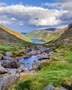 a river running through a lush green valley under a cloudy sky with mountains in the background