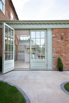 Beige Dijon limestone tiles leading up to a light green doorway surrounded by red brick. Quorn Stone, Kitchen Orangery, Limestone Patio, Terrace Interior, Limestone Floor, Orangery Extension, Limestone Pavers