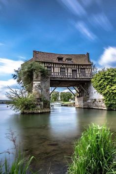 an old bridge over a body of water with a house on the top and trees around it