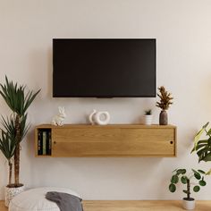 a flat screen tv mounted on the wall above a wooden shelf next to potted plants