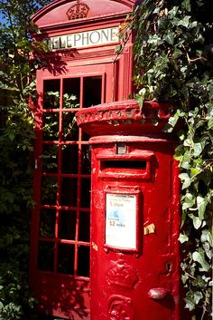 a red phone booth sitting next to a bush