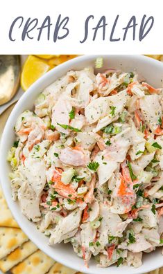 a white bowl filled with crab salad next to crackers and lemon wedges on the side