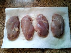 four pieces of raw chicken sitting on top of a paper towel