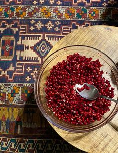 a bowl filled with pomegranate on top of a wooden table next to a rug