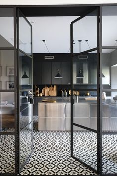 an open glass door leading into a kitchen with black and white floor tiles on the walls