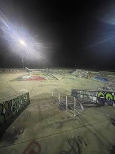 an empty skate park at night with graffiti on the ground and lights in the background