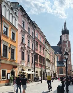 people are walking down the street in front of some buildings with tall spires on top