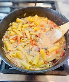 a skillet filled with pasta and vegetables cooking on the stove top next to a wooden spoon