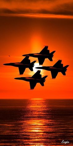 four fighter jets flying in formation over the ocean at sunset