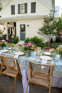 an outdoor table set with flowers and plates on it for a formal dinner outside in front of a white house