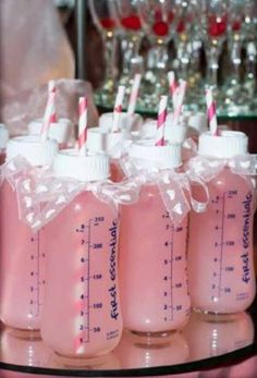 four baby bottles with straws in them on a glass table next to wine glasses