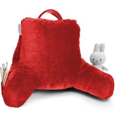 a stuffed animal sitting on top of a red pillow next to a pencil holder and an empty bag