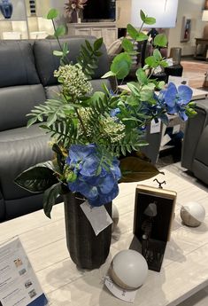 a vase with blue flowers and greenery sits on a table in a living room