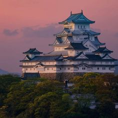 a large white building sitting on top of a lush green hillside under a pink sky