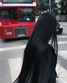 a woman with long black hair standing in front of a red bus on the street