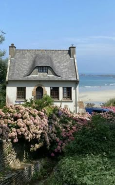 a small house with a thatched roof next to some flowers and trees on the beach