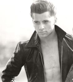 black and white photograph of man in leather jacket looking at camera with hand on hips