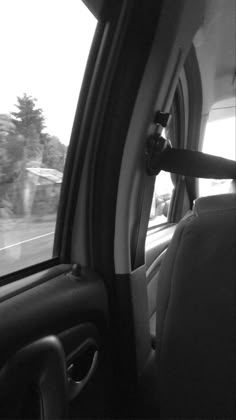 black and white photograph of the inside of a car looking out the window at trees