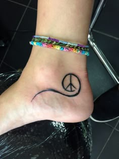 a person with a peace sign tattoo on their foot and a beaded bracelet around the ankle