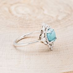 a ring with a blue stone in the center on a wooden surface, sitting on top of a piece of wood