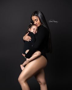 a woman holding a baby in her arms and posing for the camera with black background