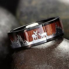 a wooden ring with deer and pine trees inlayed to it on top of a rock