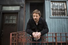 a man leaning on a railing in front of a building with blue doors and windows