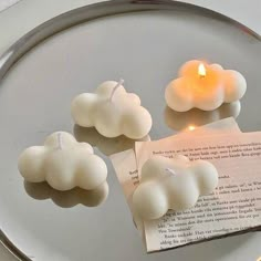 three candles sitting on top of a glass plate next to a piece of paper and a lit candle