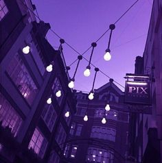 there are many lights hanging from the wires in this city street at night, and one is lit up with white bulbs