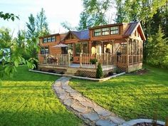 a log cabin sits in the middle of a lush green yard with a stone path leading to it