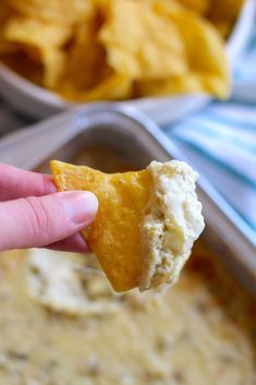 a hand holding a tortilla chip over a bowl of dip